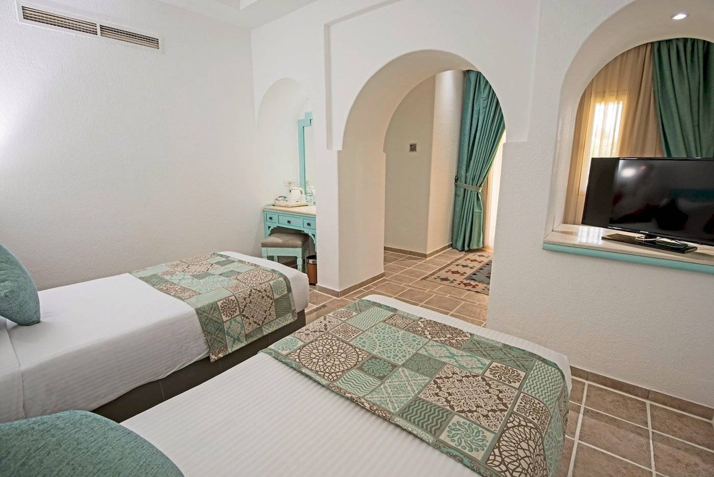 Zwei Doppelbetten mit blauen Kissen in einem eleganten Zimmer des Sunrise Royal Makadi Resorts.
