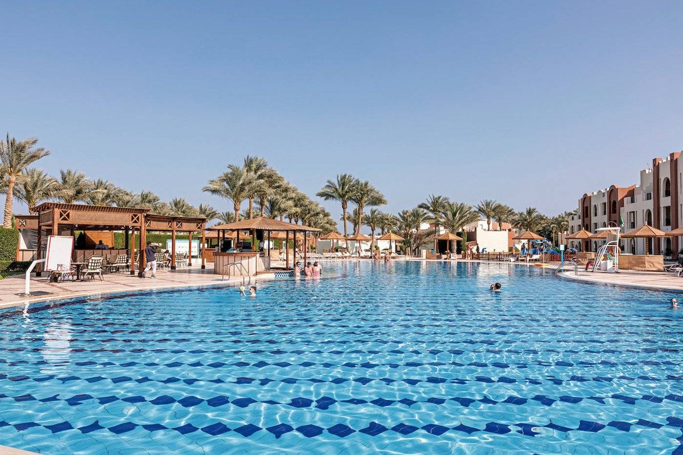 Außenpool im SUNRISE Royal Makadi Resort mit mehreren Schwimmern und Sonnenschirmen.