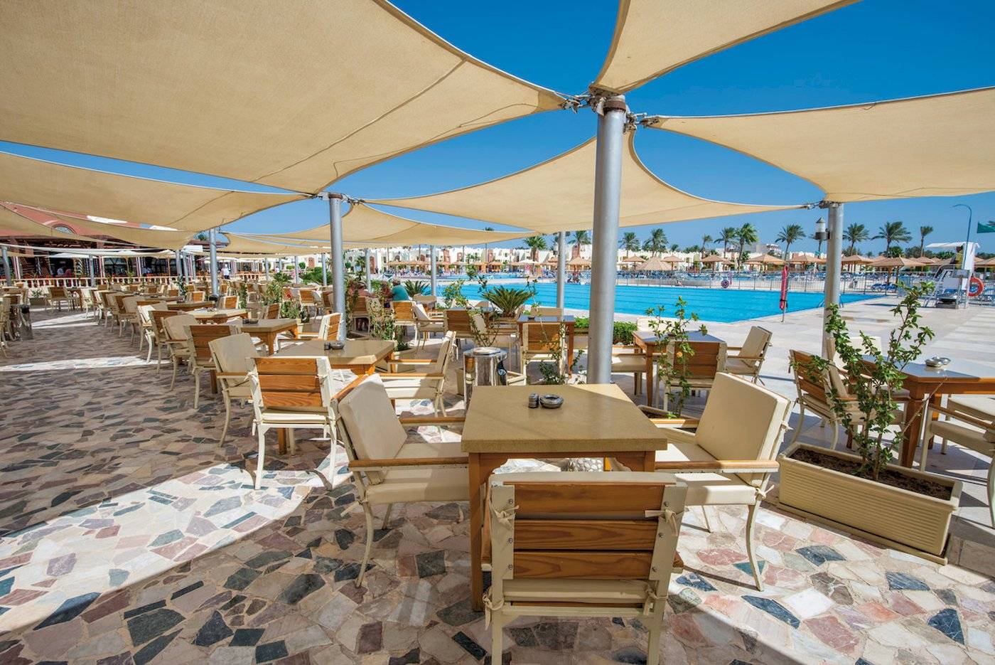 Außenbereich des Sunrise Royal Makadi Resorts mit Tischen, Stühlen und Sonnenschirmen.