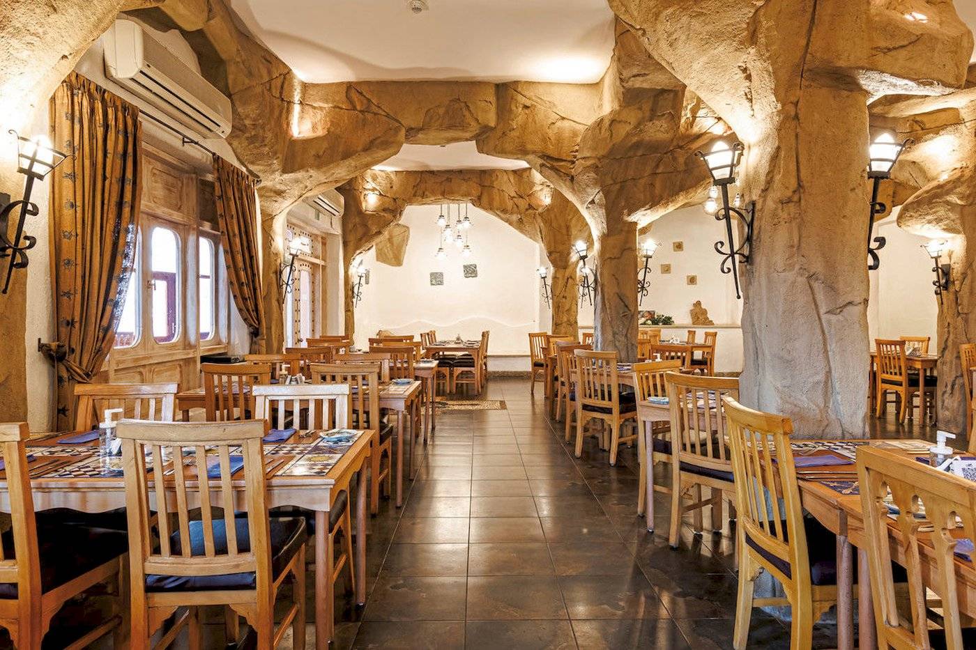 Innenbereich des Restaurants im SUNRISE Royal Makadi Resort mit Holztischen, Stühlen und steinernen Säulen.