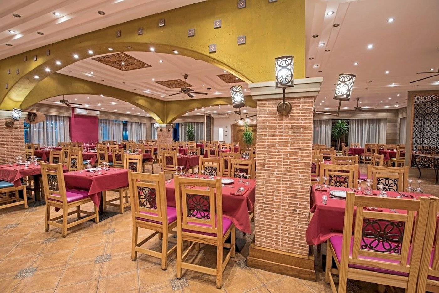 Innenbereich des Restaurants des Sunrise Royal Makadi Resort mit gedeckten Tischen, Holzstühlen und gemusterten Kissen.