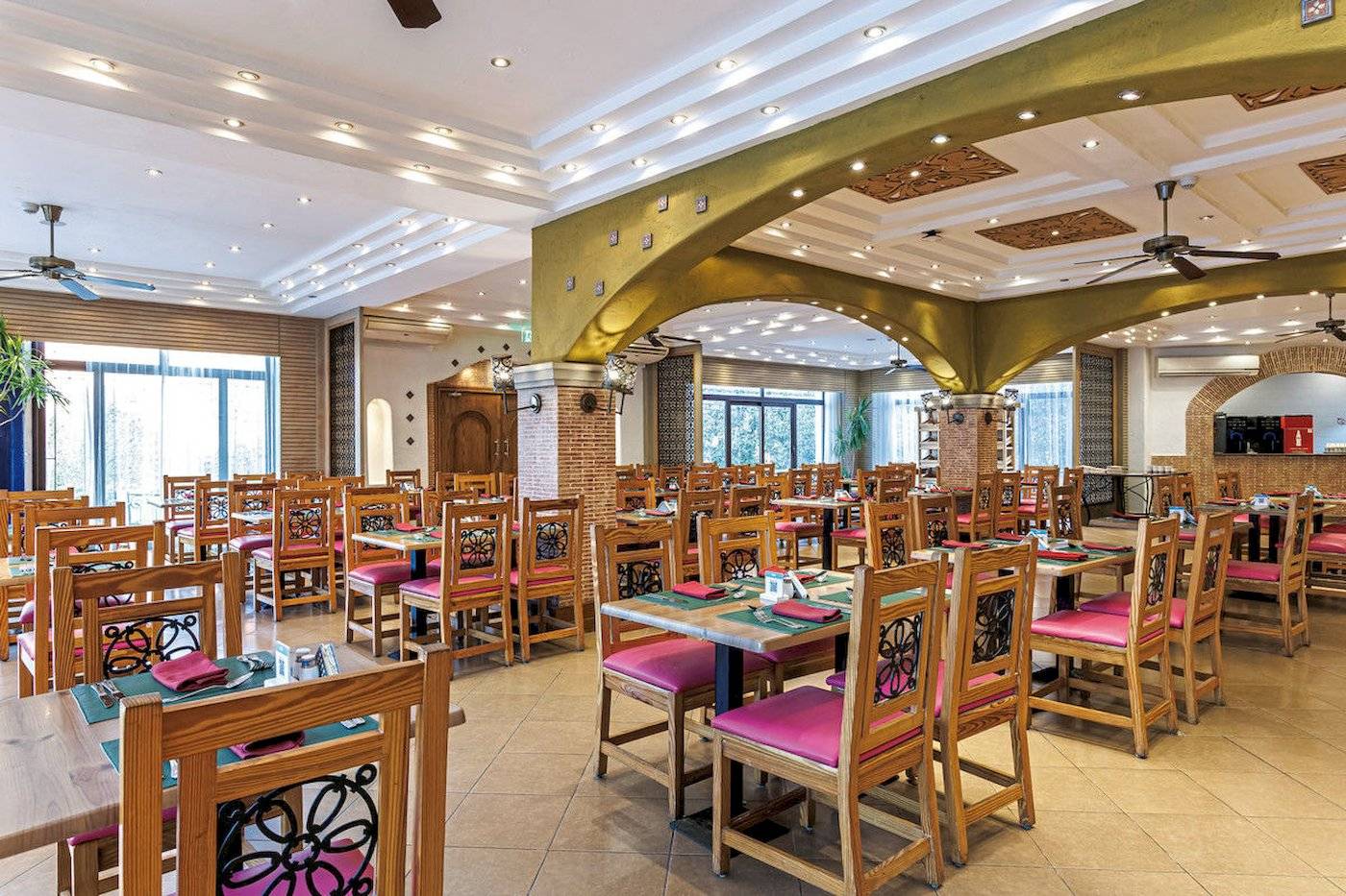 Innenbereich des Restaurants im Sunrise Royal Makadi Resort mit Holztischen und Stühlen, Deckenventilatoren und beleuchteten Decken.