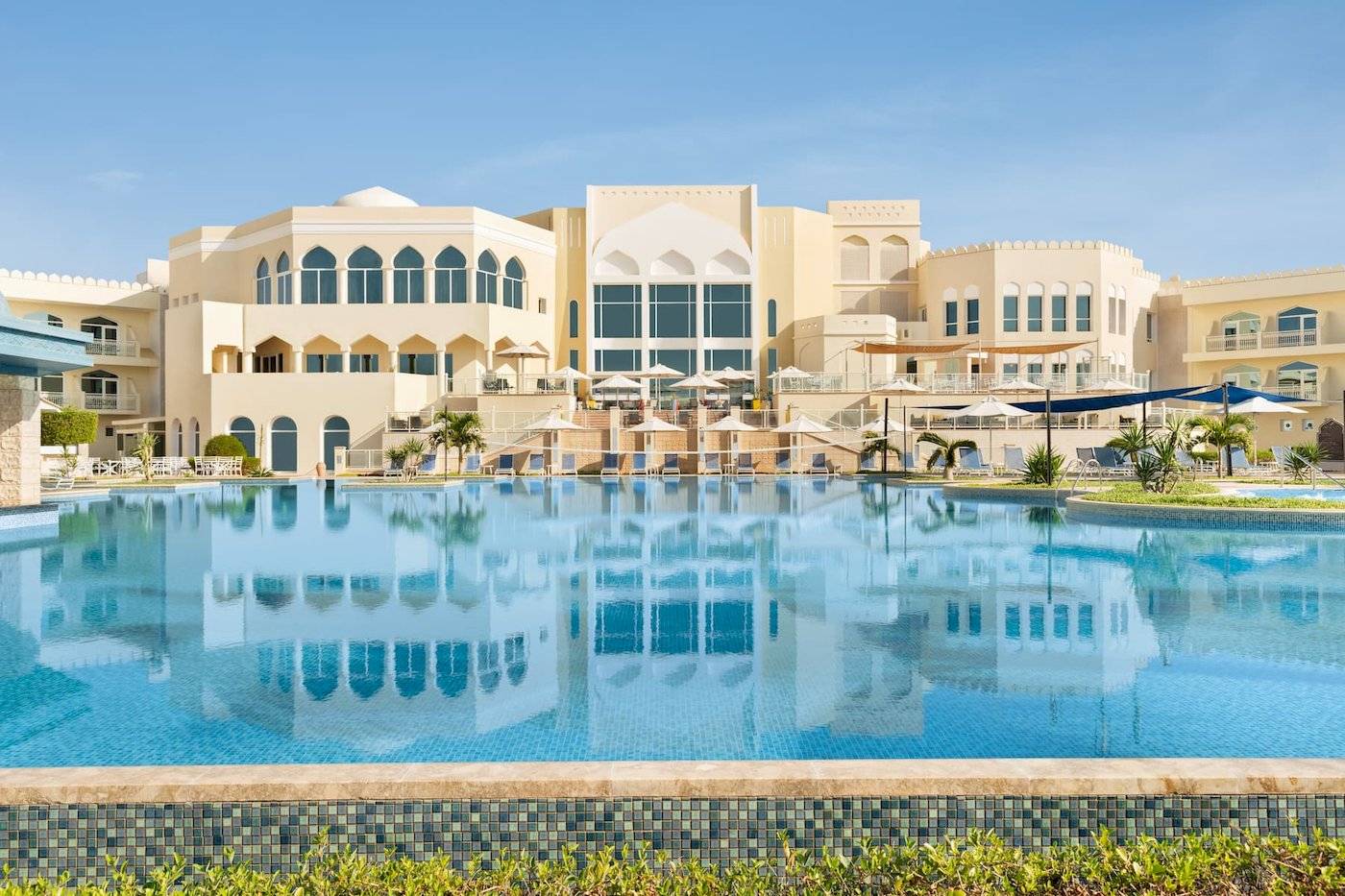 Außenbereich des Wyndham Garden Salalah Mirbat Hotels mit großem Pool und Sonnenschirmen.