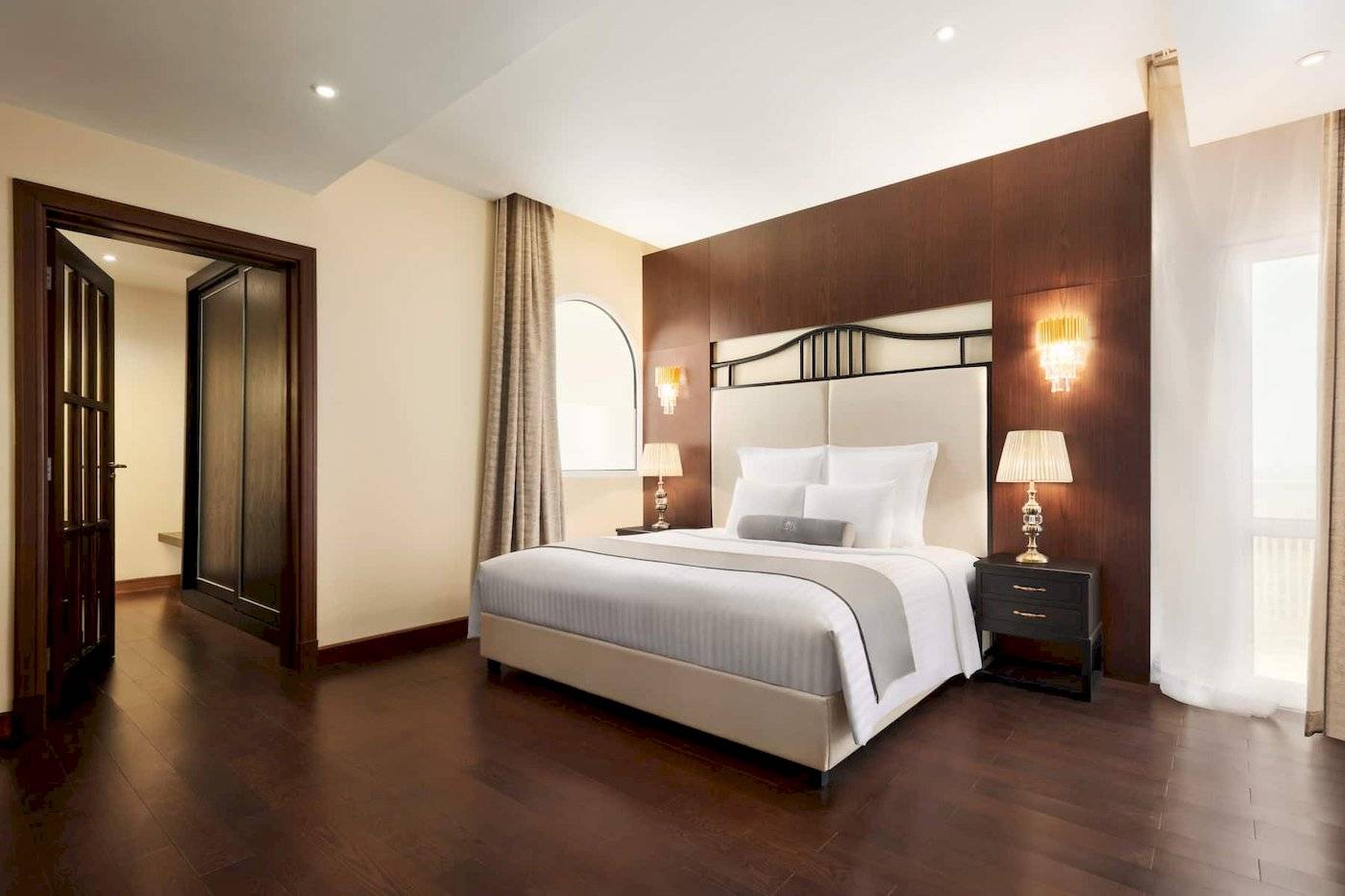 Schlafzimmer im Wyndham Garden Salalah Mirbat Hotel mit Doppelbett, Nachttischen und Lampen.