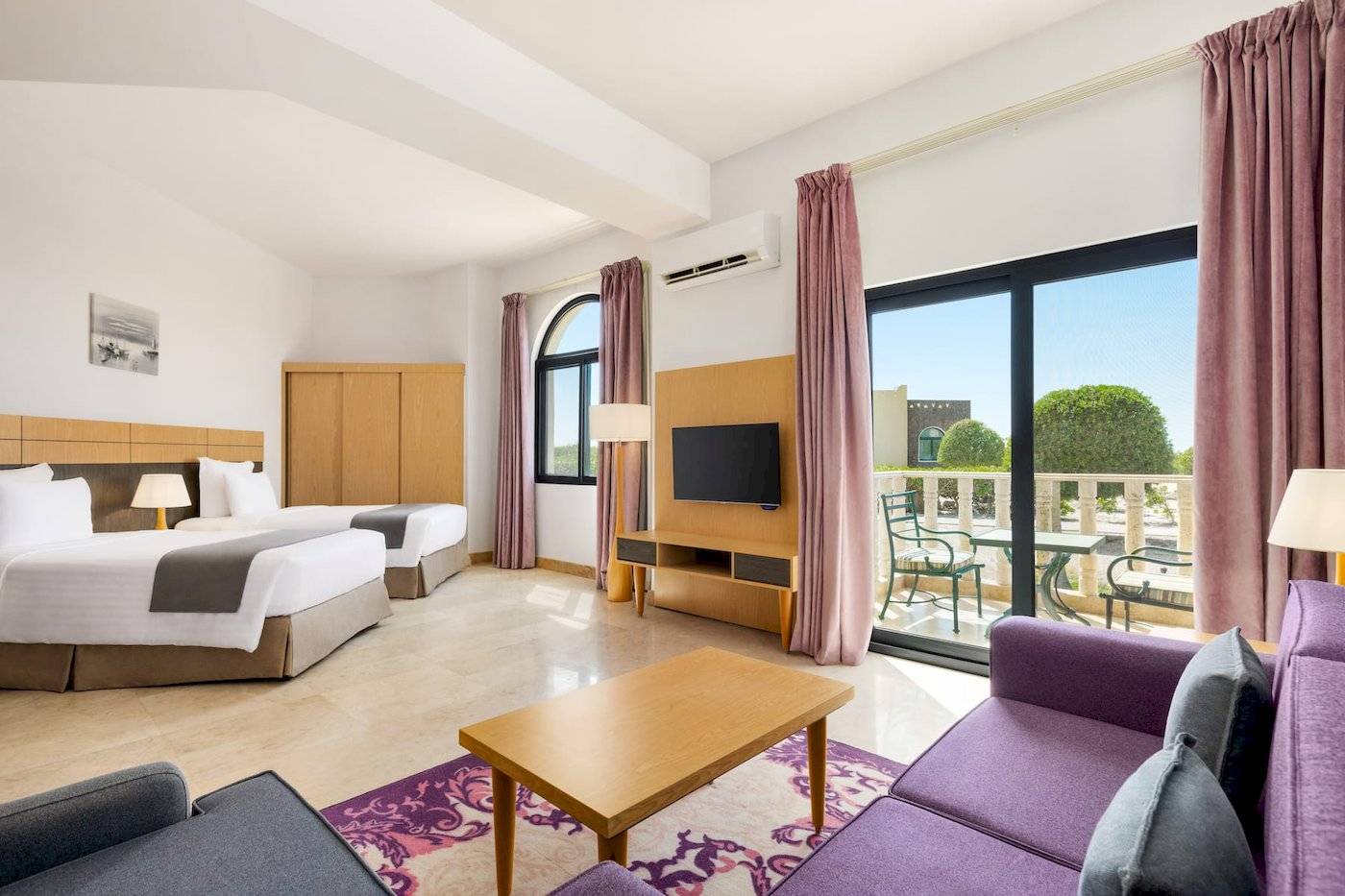 Wyndham Garden Salalah Mirbat Hotelzimmer mit zwei Betten, Fernseher, Tisch und Sofas.