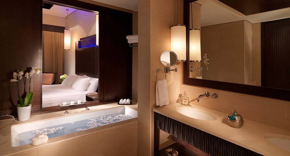 Badezimmer im Anantara The Palm Dubai Resort mit Badewanne, Spiegel und Doppelbett im Hintergrund.