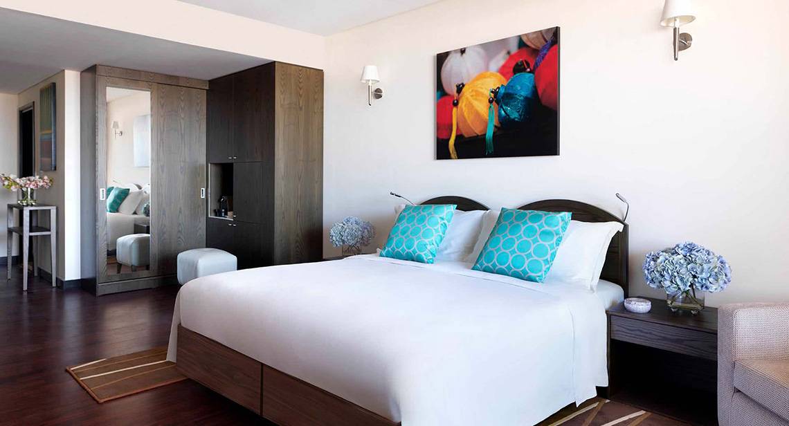 Schlafzimmer im Anantara The Palm Dubai Resort mit großem Bett, bunten Kissen und Gemälde an der Wand.
