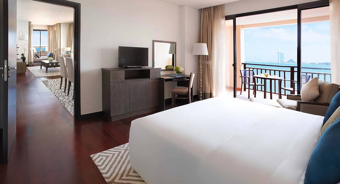 Innenansicht eines Hotelzimmers im Anantara The Palm Dubai Resort mit einem großen Bett, einem Schreibtisch, einem Fernseher und einer Terrasse mit Meerblick.