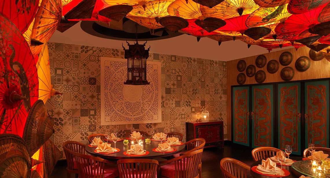 Inneneinrichtung des Anantara The Palm Dubai Resort mit rotem und gelbem Sonnenschirmen an der Decke, gemusterten Wänden und Tisch mit Kerzen.