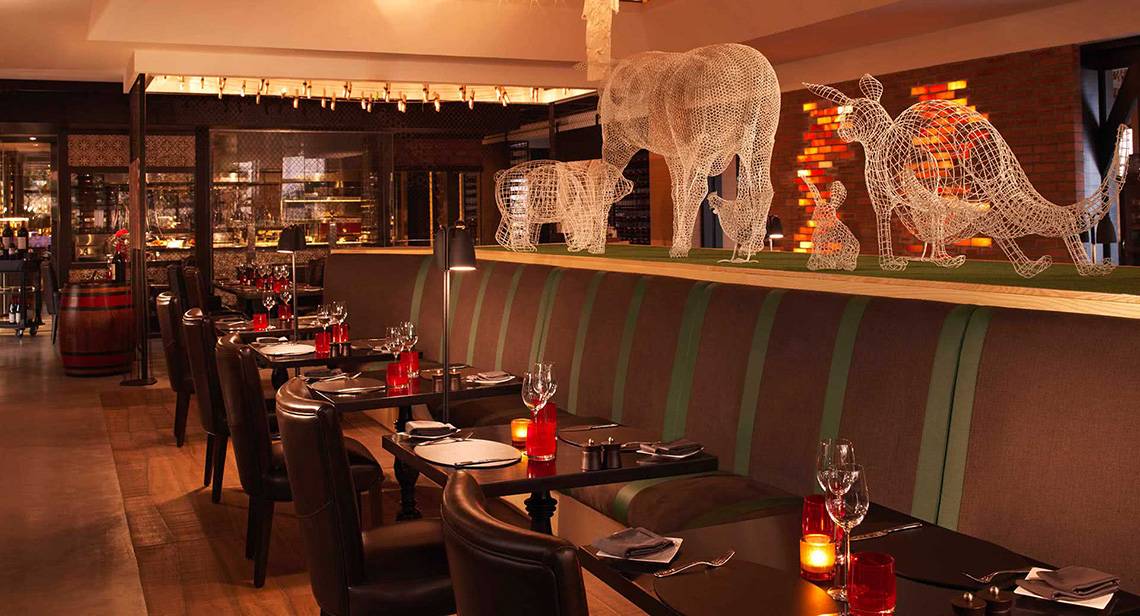 Innenansicht des Restaurants im Anantara The Palm Dubai Resort mit Tisch, Stühlen und Tierskulpturen an der Wand.