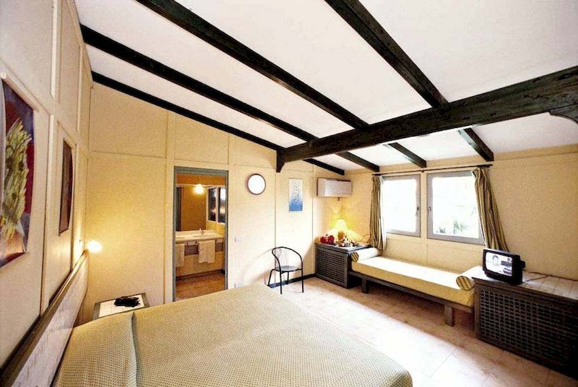 Schlafzimmer im VOI Vila Do Farol Resort mit einem großen Bett, einer Bank, einem Fernseher und einer Lampe.