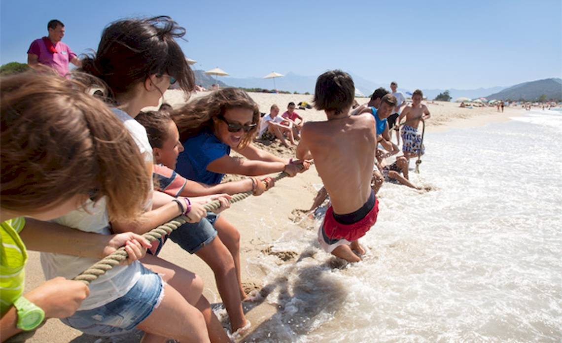 Kinder ziehen einen Jungen am Strand im Wasser an einem Seil