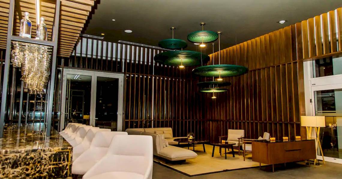 Das geräumige Lounge- und Barbereich des Melia Caribe Beach Resort mit weißen Möbeln, Holzwänden und grünen Hängelampen.