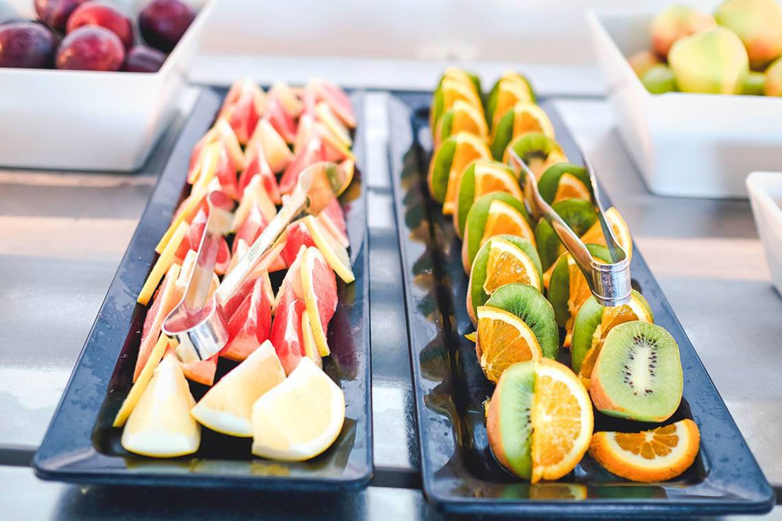 Obstbuffet im Creta Royal Hotel mit Wassermelonen, Orangen, Kiwis und Zitronen auf schwarzen Tabletts.