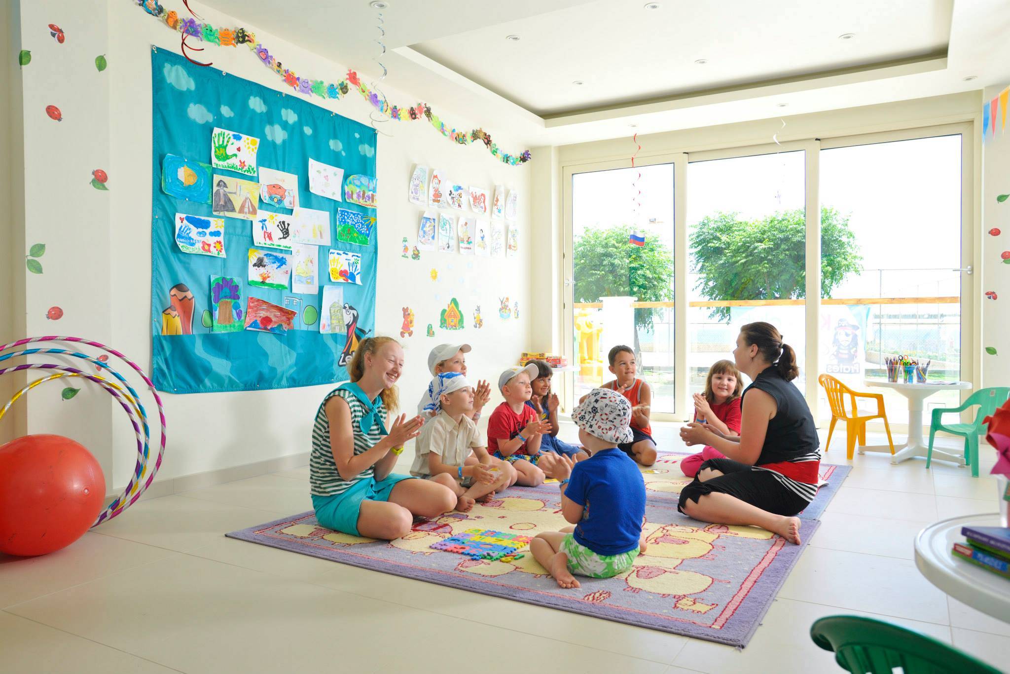 Gruppe von Kindern und zwei Erzieherinnen, die eine Runde sitzen und singen, im Pernera Beach Hotel.