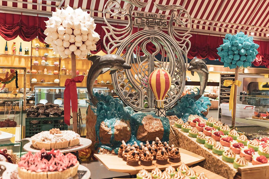 Buffet im 'Land der Legenden Königreich' Hotel mit einer Statue, Heißluftballon und verschiedenen Kuchen und Desserts.