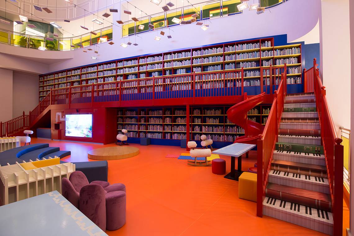 Innenansicht der Bibliothek im Land of Legends Kingdom Hotel mit roten Treppen, Bücherregalen und bunten Möbeln.