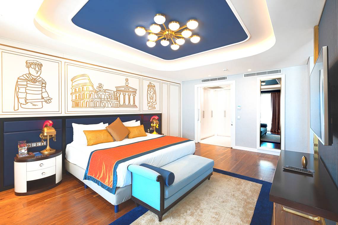 Hotelzimmer im Land of Legends Kingdom mit blauer Decke, römischen Wandmalereien und luxuriösem Bett.