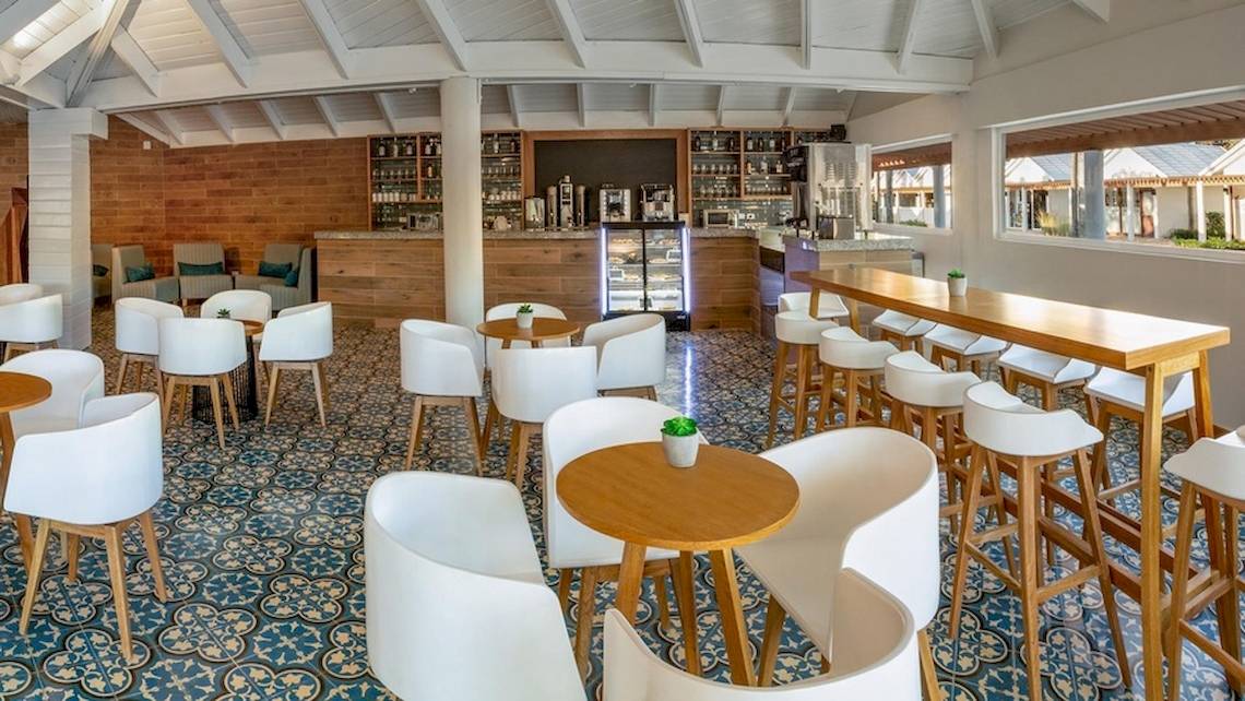 Innenansicht des Grand Sirenis Punta Cana Resorts mit Loungebereich, Bar, Tischen und Stühlen.