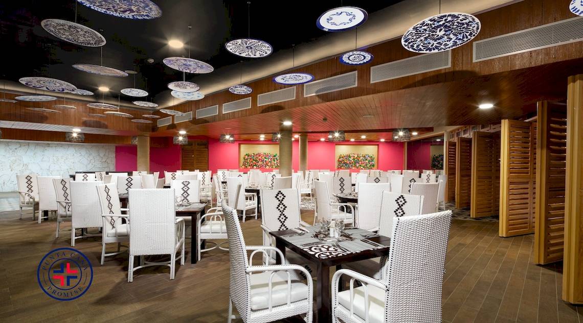 Innenansicht des Restaurants im Grand Sirenis Punta Cana Resort mit weißen Stühlen und Tischen.
