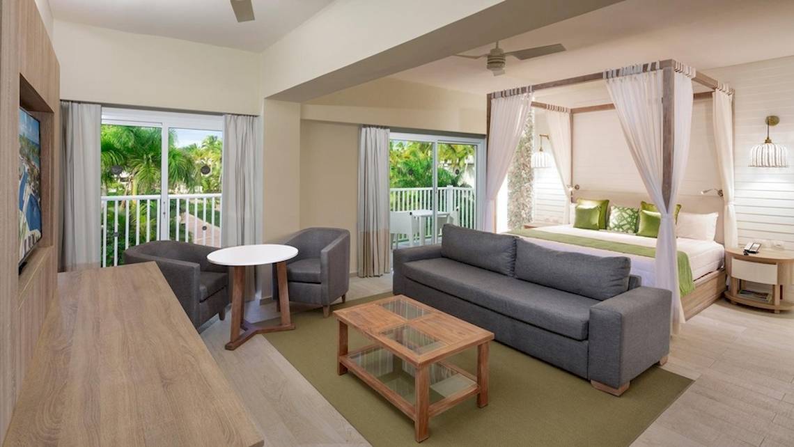 Innenansicht einer Suite im Grand Sirenis Punta Cana Resort mit Wohnzimmer und Schlafzimmerbereich.