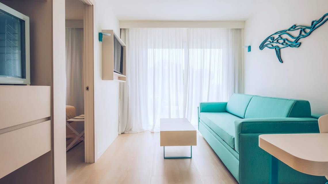 Ein modernes Hotelzimmer im Iberostar Waves Alcudia Park mit einer blauen Couch, einem Couchtisch und einem Fernseher.