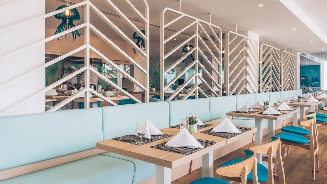 Innenbereich des Iberostar Waves Alcudia Park Hotels mit hellblauen Sofas, Holztischen und geometrischen Wanddesigns.