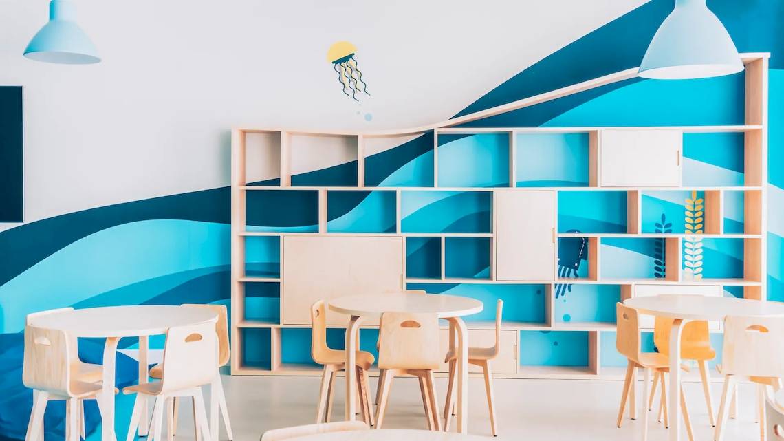 Kinderzimmer im Iberostar Waves Alcudia Park mit blauen und weißen Wänden, einem Bücherregal, und runden Tischen und Stühlen.