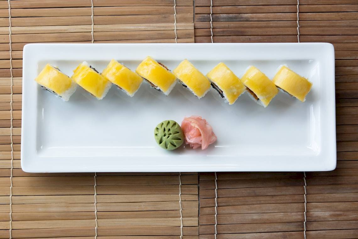 Ein weißer Teller mit verschiedenen Sushi-Rollen, darunter eine grüne und eine rosa Rolle.