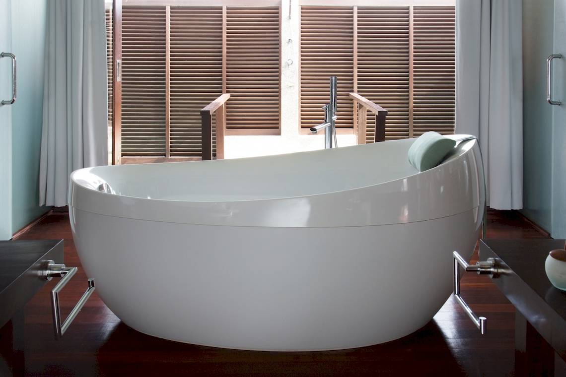 Ein weisses Badewanne im Badezimmer von Coco Bodu Hithi mit einem Fenster im Hintergrund.
