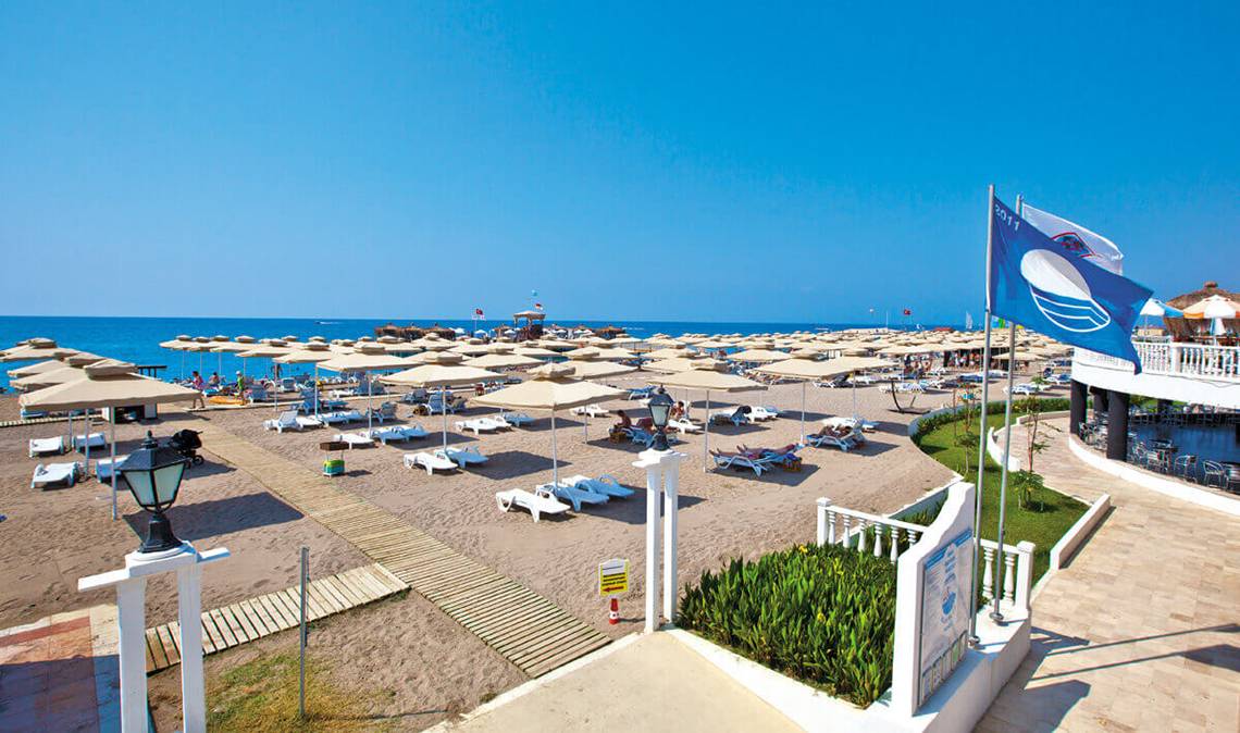 Club Nena Hotel Strand mit Sonnenschirmen und Liegestühlen unter blauem Himmel