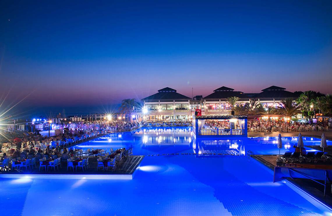 Abendansicht des Poolbereichs des Club Nena Hotels mit beleuchtetem Wasser und Gästebereichen.