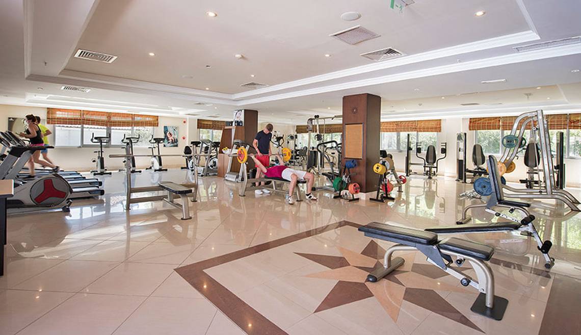 Fitnesscenter im Club Nena Hotel mit verschiedenen Geräten und aktiven Gästen.