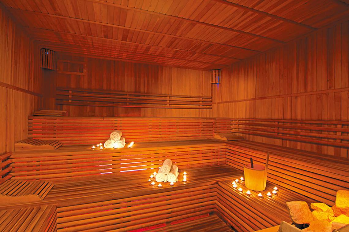 Innenansicht der Sauna im Club Nena Hotel mit Holzbänken, warmem Licht und Dekorationsgegenständen.