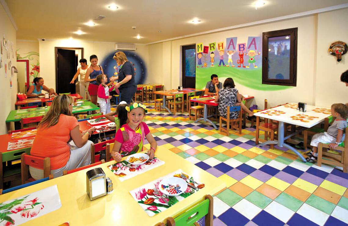 Club Nena Kinderfrühstücksbereich mit bunten Tischdecken und Wandmalerei.