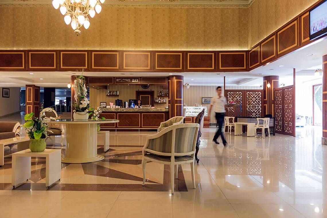Empfangsbereich des Club Nena Hotels mit Bar, Tischen und Stühlen, ein Mann geht vorbei.