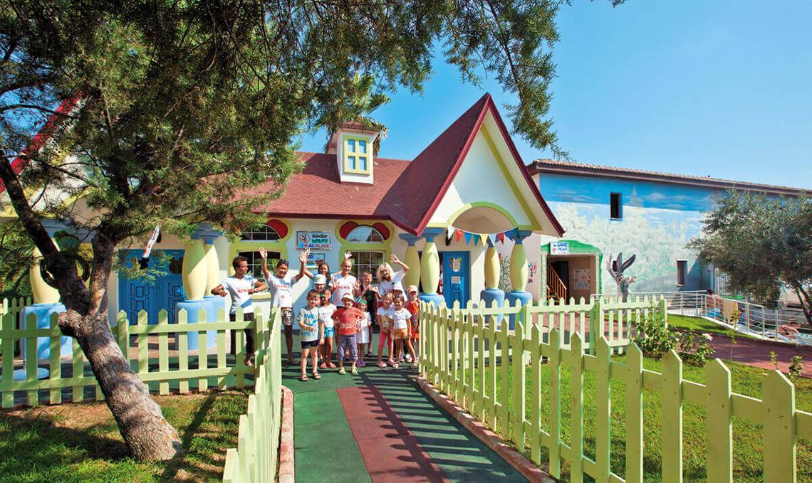 Gruppe von Kindern und Erwachsenen im Club Nena Kinderclub vor einem bunten Gebäude.