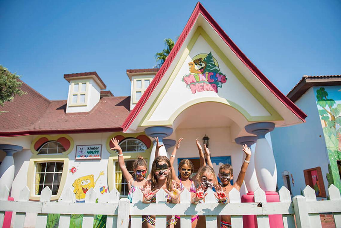 Kinder vor einem bunten Haus des Club Nena mit Masken auf den Händen.