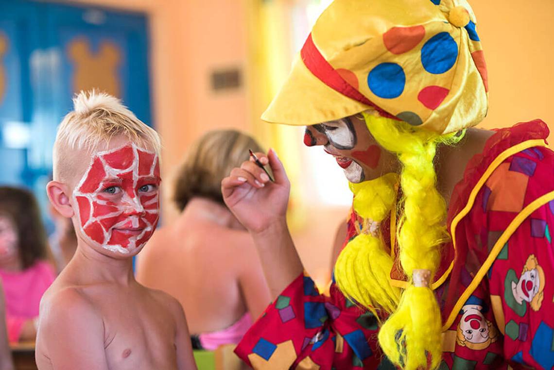 Ein Clown malt das Gesicht eines Jungen im Club Nena Hotel.