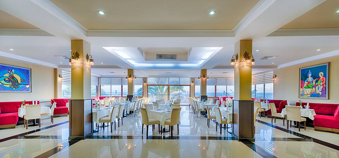 Innenansicht des Restaurants des Club Nena Hotels mit gedeckten Tischen und Stühlen, Blick auf das Meer.