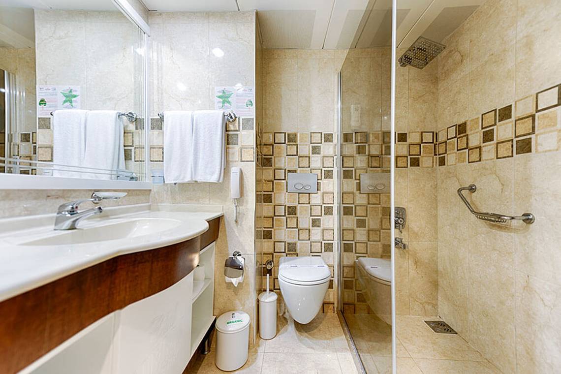 Badezimmer im Club Nena Hotel mit gefliester Wand, Dusche, Toilette und Waschbecken.