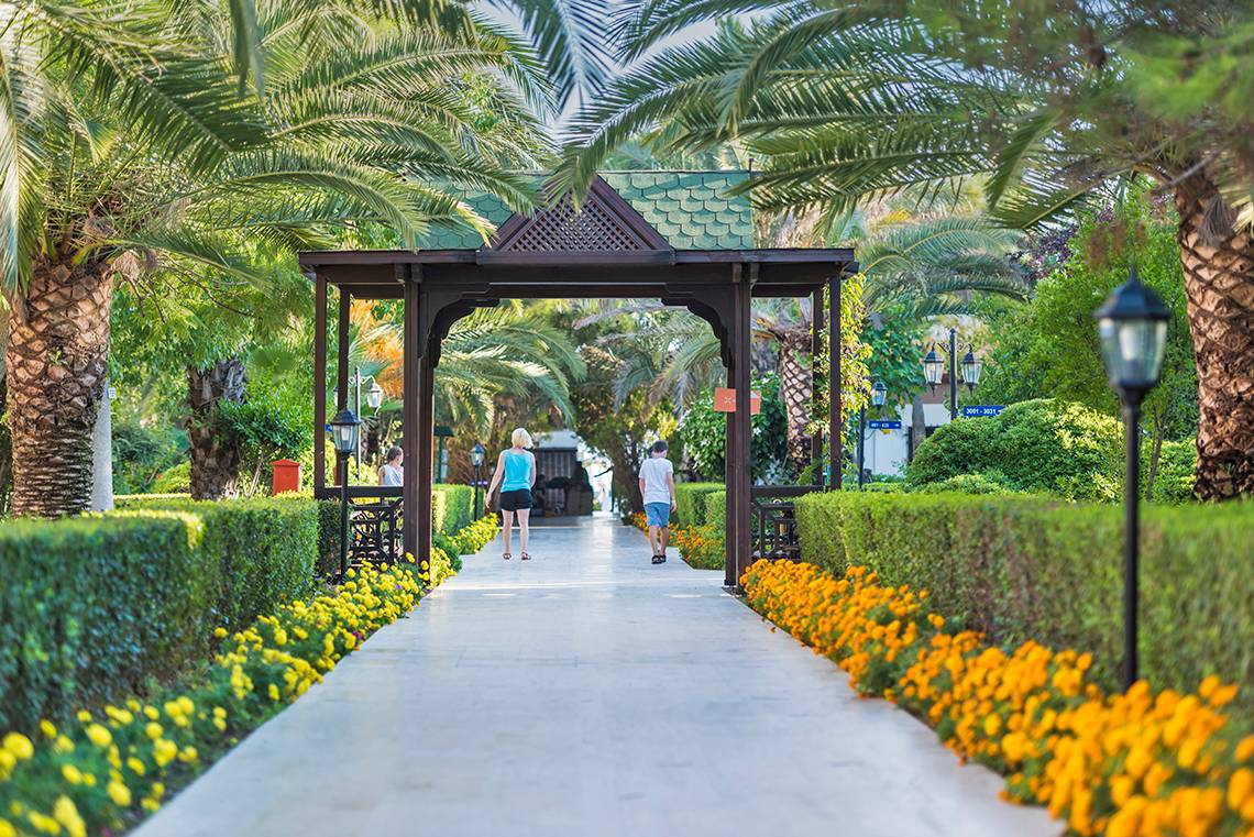 Gartenweg zum Eingangsbereich des Club Nena Hotels mit zwei Personen und Palmen.