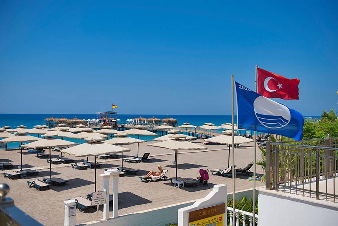 Strand des Club Nena Hotels mit Sonnenschirmen, Liegen und Flaggen