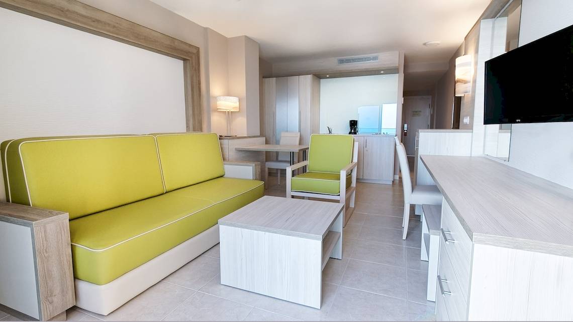 Inneneinrichtung eines Hotelzimmers im Bull Dorado Beach & Spa Hotel mit gelbem Sofa, Tisch und Fernseher.