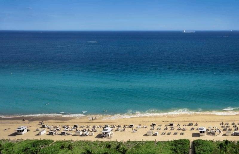 Luftaufnahme des Fontainebleau Miami Beach mit Strand, Meer und Liegestühlen.