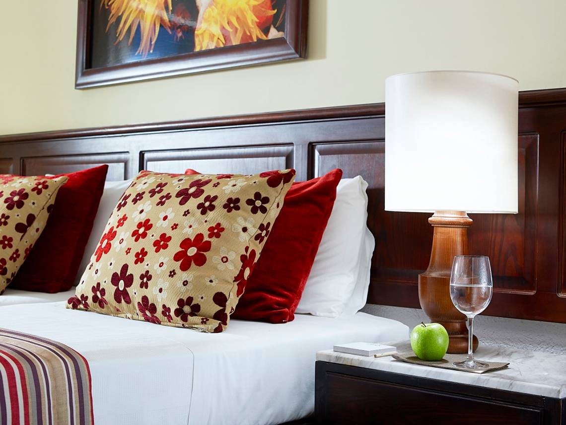 Bett im Albatros Spa & Resort mit Kissen, Lampen und Tisch mit Glas Apfel und Weinglas