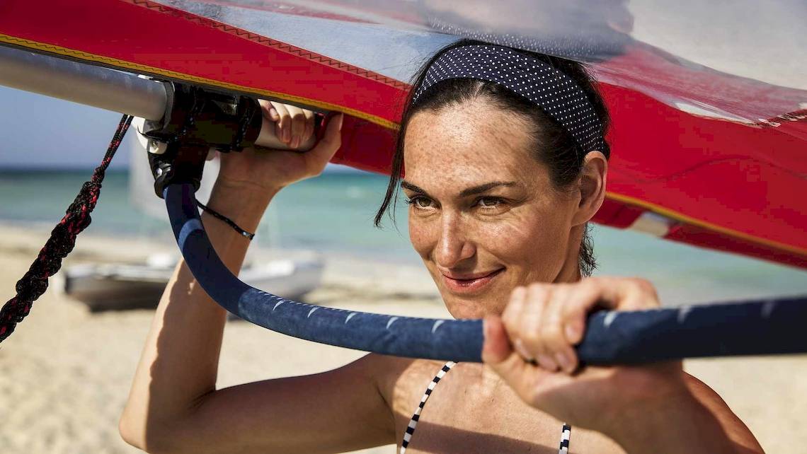 Frau auf dem Strand mit einem Segelboot, das sie in die Luft hebt.