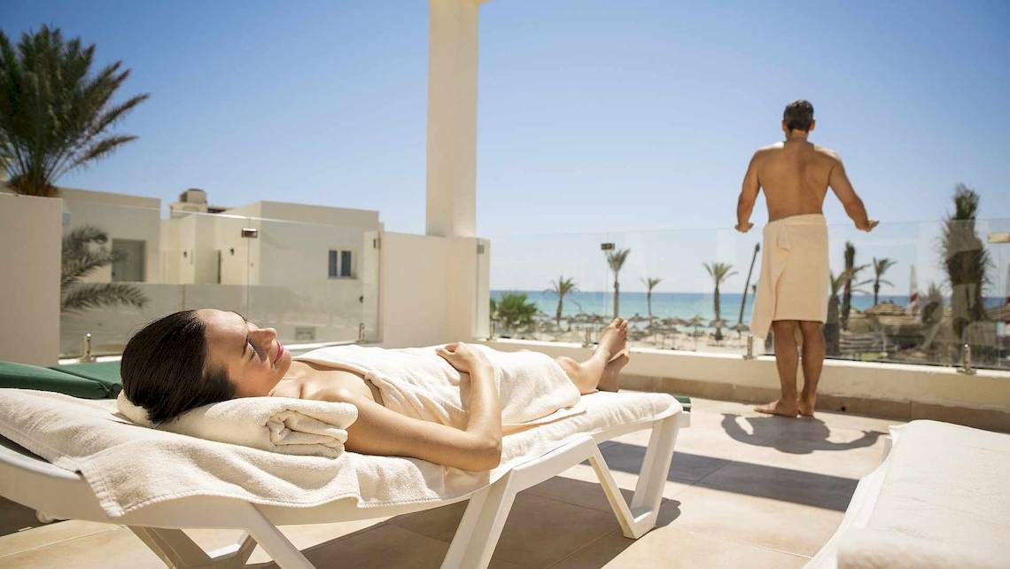 Eine Frau entspannt sich auf einem Liegestuhl auf dem Balkon des Robinson Djerba Bahiya Hotels mit Blick auf das Meer.