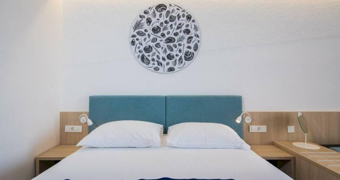 Ein Hotelzimmer im Osmine Slano mit einem Bett, zwei weißen Kissen, einem blauen Kopfteil und einer Wanddekoration.