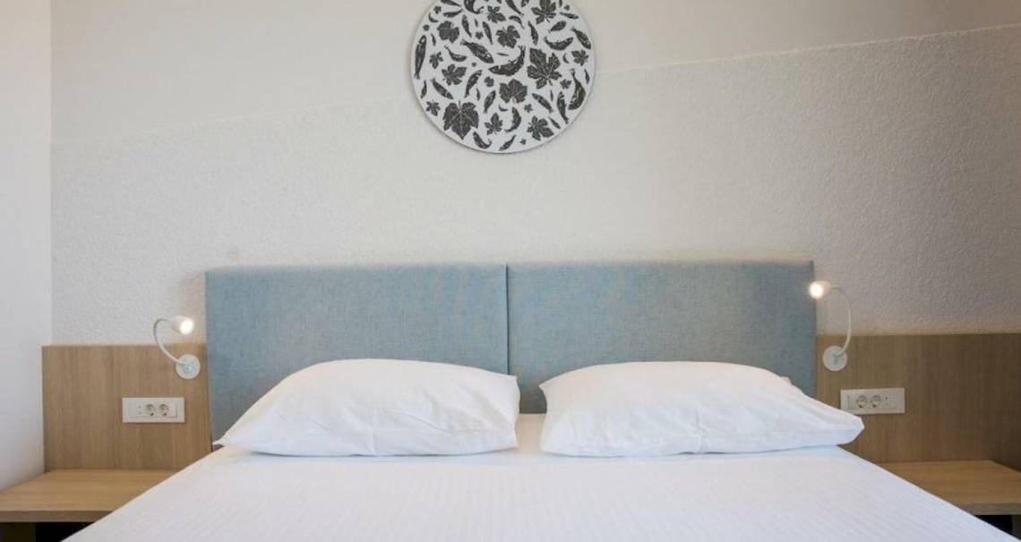 Doppelbett im Hotelzimmer von Osmine Slano mit weißen Kissen und blauen Kopfteilen.